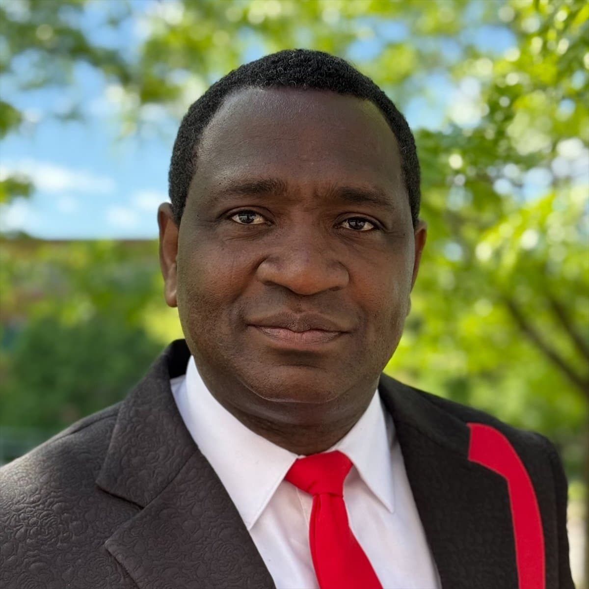 Pastor Sam Adusi outdoors in a dark suit and red tie